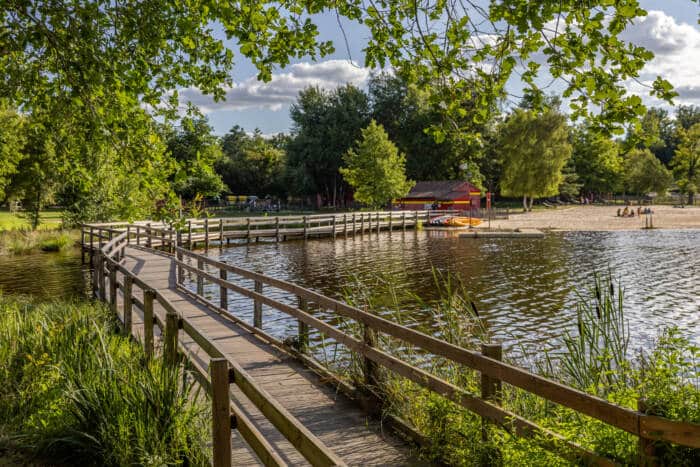 Un passerelle cheminant au-dessus d'un étang, et conduisant à une base de loisirs